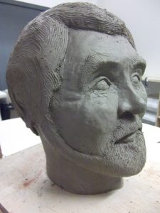 A detailed clay sculpture of a man with a beard and strong nose. The sculpture stops at his neck.