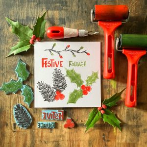 A hand printed paper is the focus of this image. Surrounding the paper is the lino cutting tools made to make the print. It is very festive.