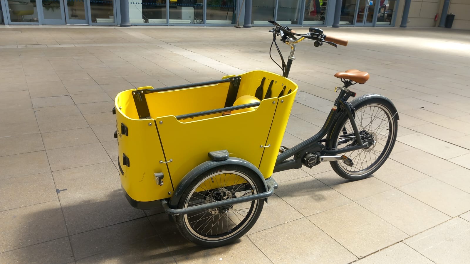 A yellow cargo bike on a concrete tiled floor.